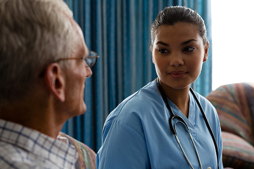 Female doctor interacting with senior man while sitting in nursing home