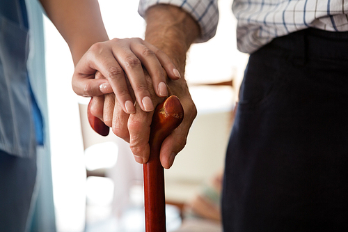 Cropped hands of female doctor and senior man holding walking cane in nursing home