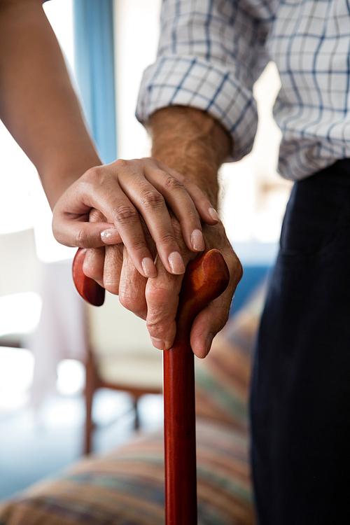 Cropped hands of female doctor and senior man holding walking cane in retirement home