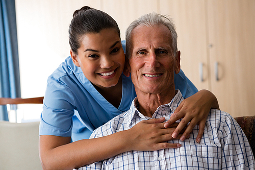 Portrait of smiling female doctor standing by senior man sitting in nursing home