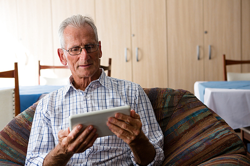 Senior man using tablet computer while sitting on armchair in nursing home