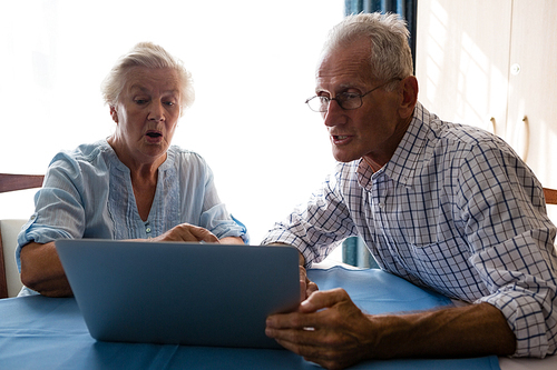 Senior man showing laptop to female friend at table in nursing home