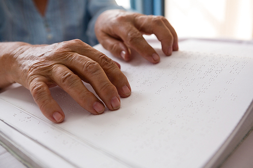 Cropped hands of senior woman reading braille in nursing home