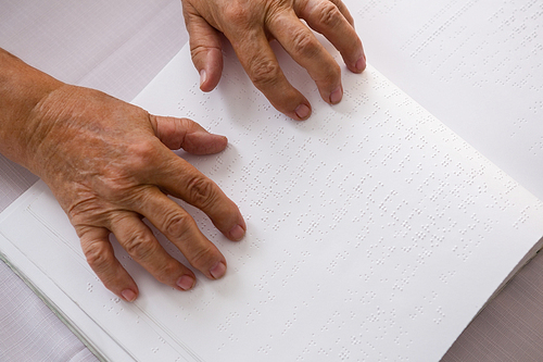 Overhead cropped hands of senior woman reading braille in nursing home