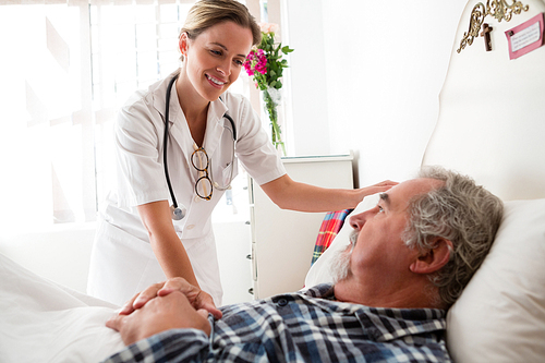 Female doctor examining senior man lying on bed in nursing home