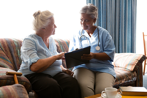 Senior woman discussing with doctor while reading book sofa in nursing home