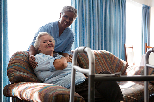 Portrait of smiling nurse with senior woman at sofa in nursing home