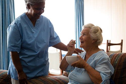 Senior woman talking to nurse while having food in nursing home