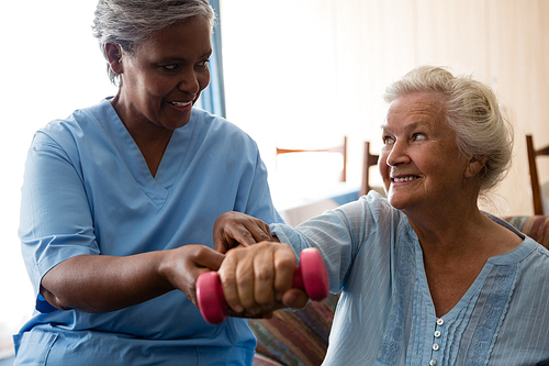 Nurse helping senior woman in lifting dumbell at nursing home