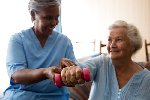 Nurse helping senior woman in lifting dumbell at retirement home