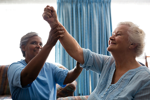 Nurse helping senior woman in flexing muscles at nursing home