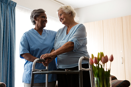 Nurse assisting senior patient in walking with walker at nursing home