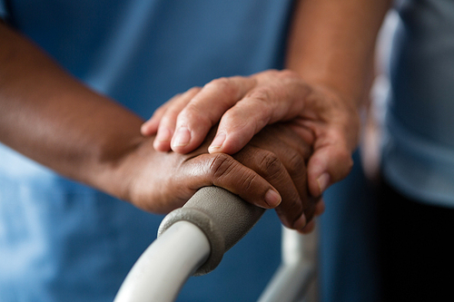 Cropped hands of nurse and senior woman holding walker in nursing home