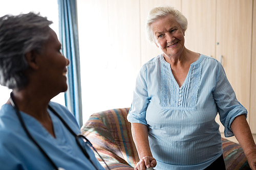 Nurse and senior woman looking at each other while standing in nursing home