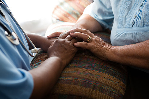 Midsection of nurse and patient relaxing at sofa in nursing home