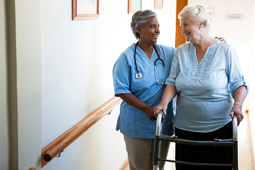 Nurse assisting senior patient in walking with walker at retirement home