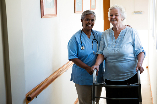 Portrait of nurse assisting senior patient in walking with walker at retirement home