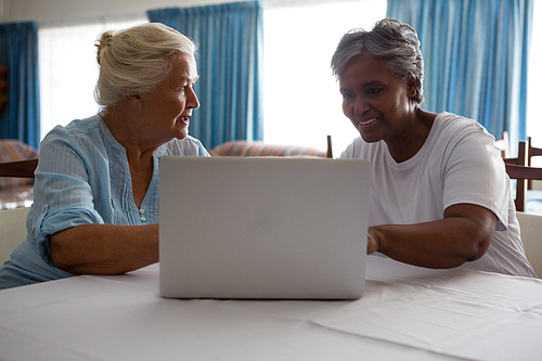 Senior woman showing laptop to friend at table in nursing home