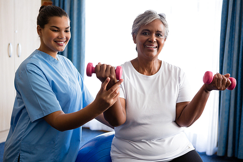 Nurse assisting senior woman in lifting dumbbells at retirement home