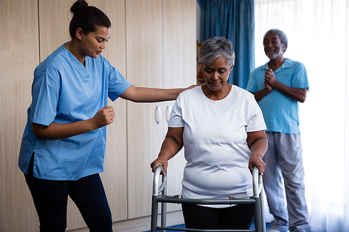 Nurse assisting senior woman in walking with walker at retirement home