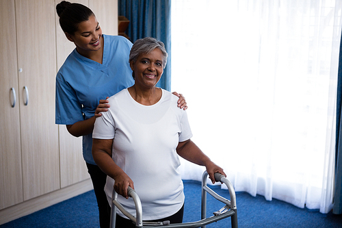 Nurse assisting senior woman in walking with walker at nursing home