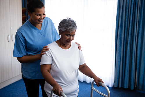 Nurse hepling senior woman in walking with walker at nursing home