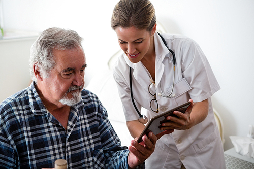 Female doctor showing digital tablet to senior man in nursing home