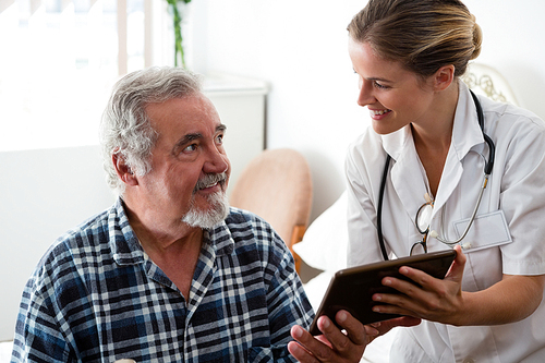 Female doctor showing digital tablet to senior man in retirement home