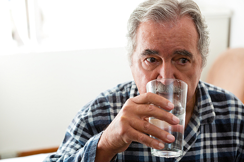 Senior man drinking water while sitting in nursing home