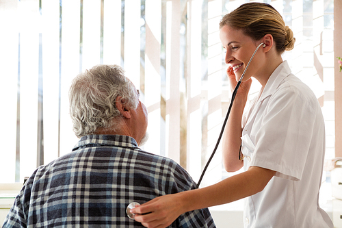 Female doctor examining senior patient with stethoscope at nursing home