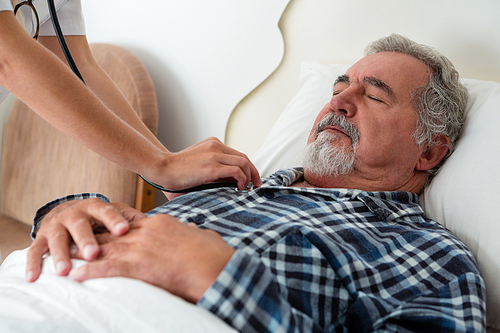 Cropped hands of doctor listening to heartbeats of senior man sleeping on bed in retirement home