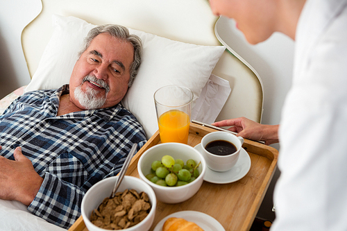 Cropped hand of female doctor serving food to senior patient relaxing on bed in nursing home