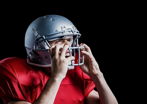 Aggressive american football player holding his helmet against black background