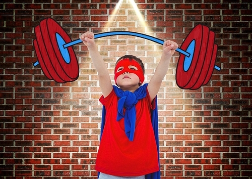 Boy in superhero costume holding a dumb bell against brick wall background