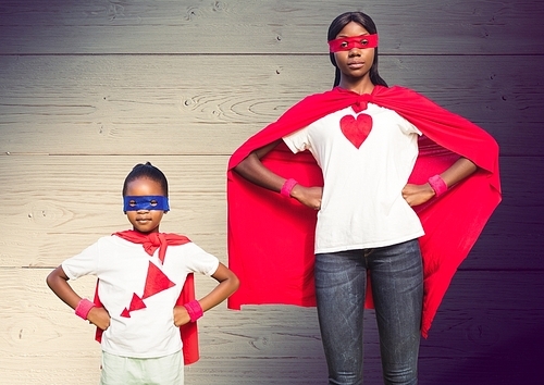 Mother and son in superhero costumes standing with hands on hips against wooden plank background