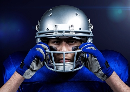 American football player adjusting his helmet against blue background