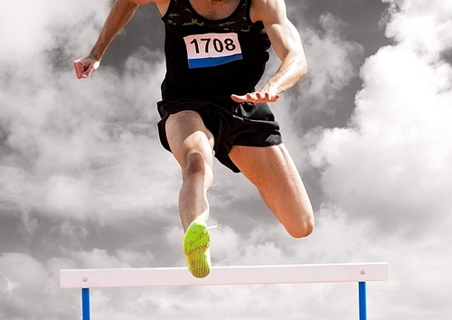Athlete running over hurdle against digitally composite cloudy sky