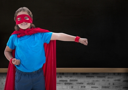 Portrait of smiling super kid in red cape and red mask standing against black background