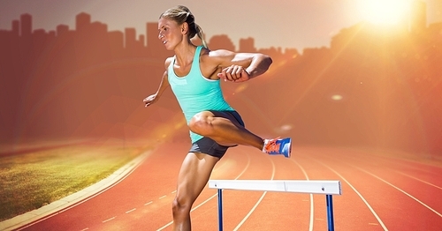 Athlete running over hurdle against digitally composite sunset stadium