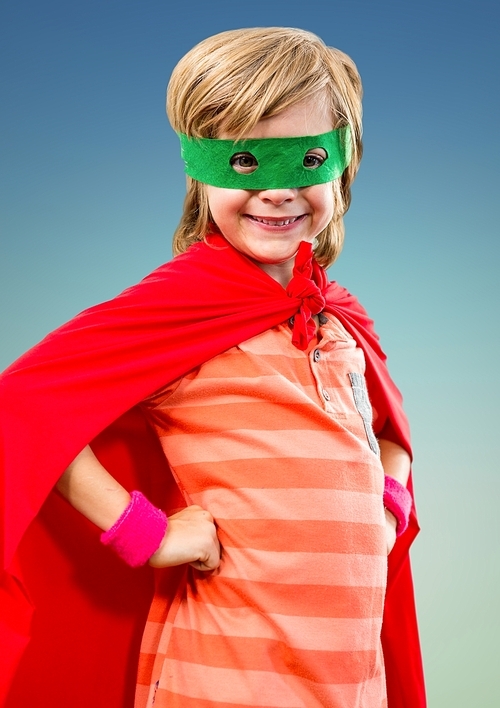 Portrait of smiling super kid in red cape and green mask standing with hand on hip
