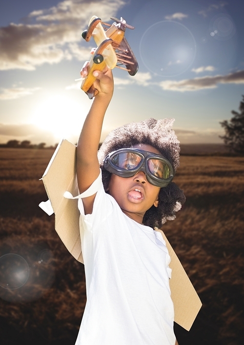 Composite image of smiling kid pretending to be a pilot in field at sunset