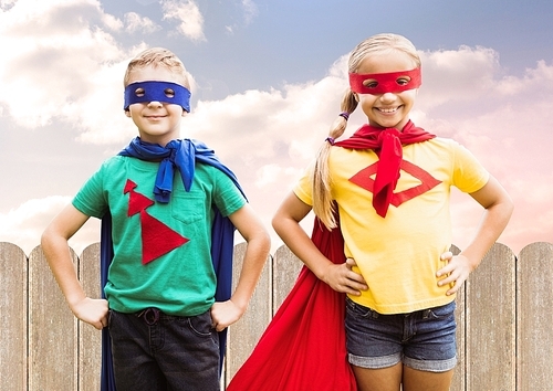 Two children wearing superhero costume standing with hands on hip against sky background