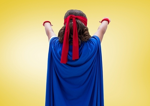 Rear view of girl wearing superhero costume standing against yellow background