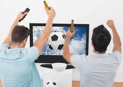 Two excited men cheering with beer bottle while watching sport match on tv at home