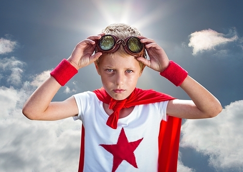 Portrait of confident boy wearing superhero costume standing against cloudy sky background