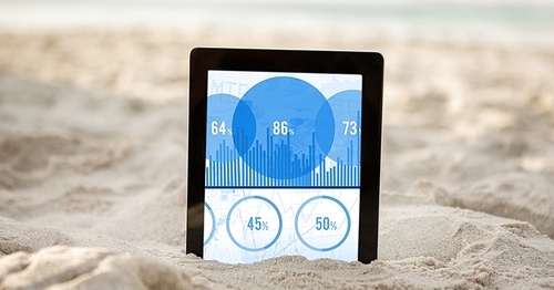 Close-up of digital tablet in sand showing percentage data