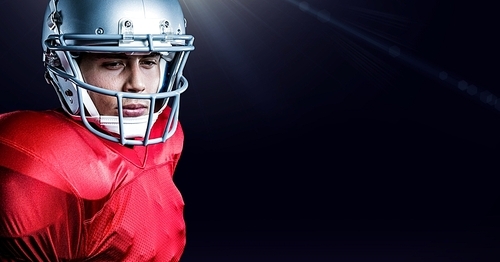 Serious american football player wearing helmet standing against black background