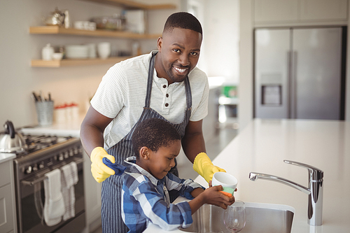 Portrait of smiling father and son cleaning cup in kitchen at home