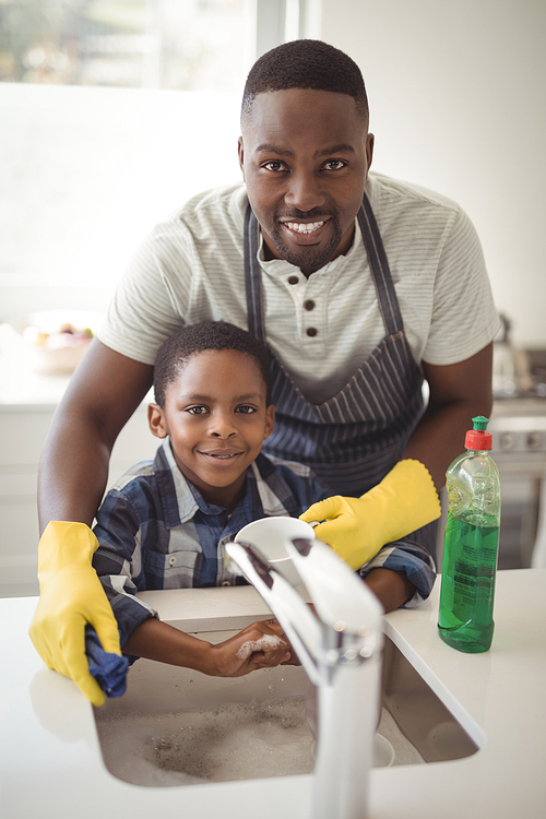 Portrait of smiling father and son cleaning utensils in kitchen at home