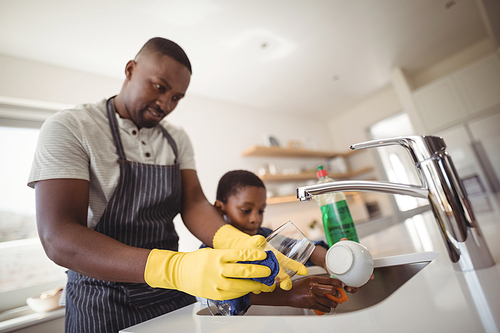 Father and son cleaning utensils in kitchen at home